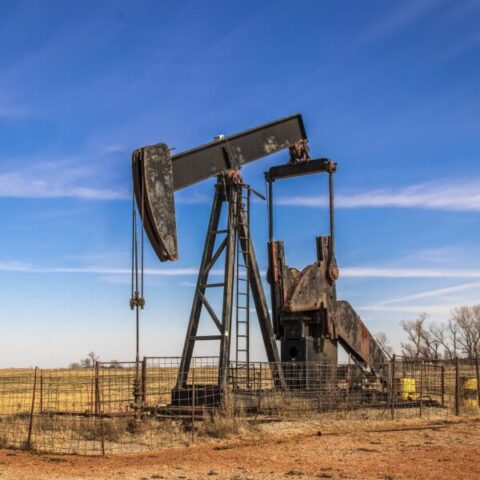 Abandoned rusty oil well pump jack surrounded by cattle fence